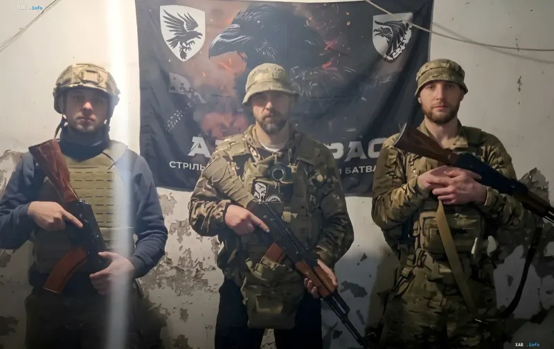 Трое украинских военных в камуфляже и с оружием на фоне флага с изображением ворона