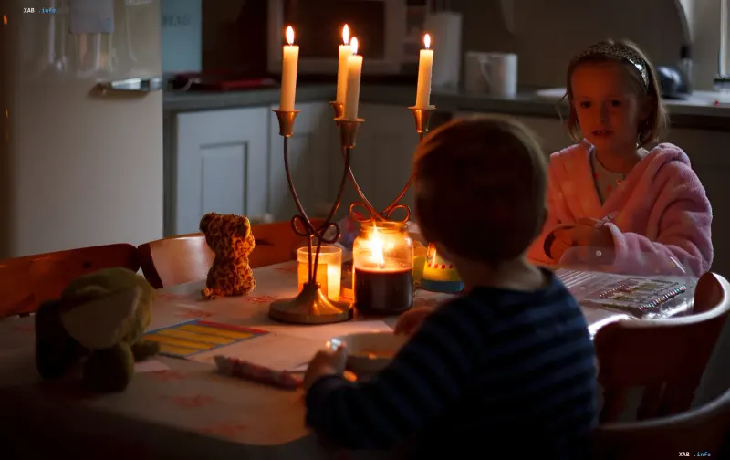 Kinder sitzen bei Kerzenschein während eines Notstromausfalls an einem Esstisch