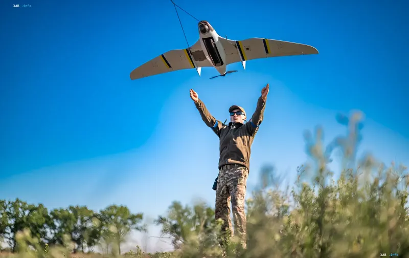 A military serviceman launching a fixed-wing reconnaissance UAV in a field under a clear blue sky