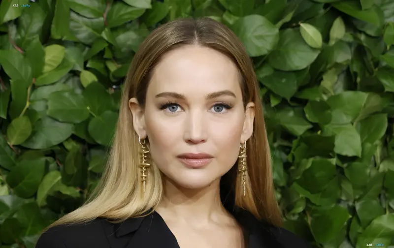 Schauspielerin Jennifer Lawrence mit blonden Haaren und schwarzem Outfit vor grünem Laub