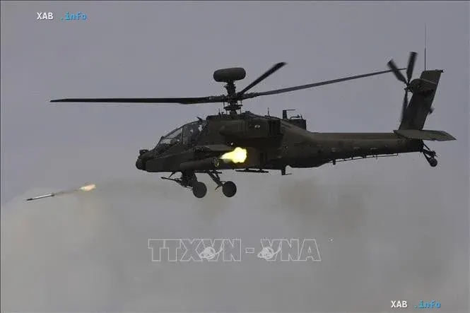 Военный ударный вертолет AH-64 Apache в полете запускает ракету в ходе учений