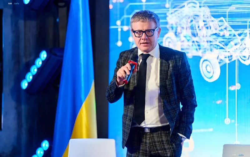 Глава Немецко-Украинской торговой палаты Райнер Перау выступает с микрофоном на фоне украинского флага