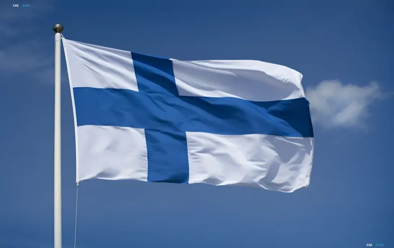 Die Flagge Finnlands weht an einem weißen Fahnenmast vor einem klaren blauen Himmel mit einer Wolke