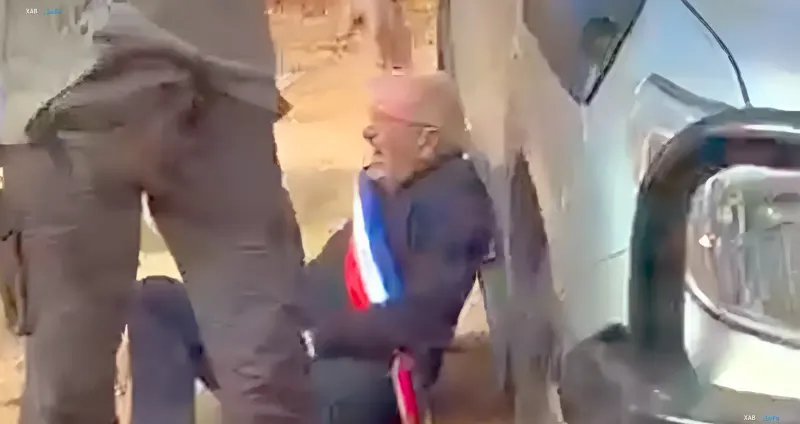 Пожилой человек с лентой в цветах французского флага лежит на земле рядом с автомобилем после нападения поселенцев