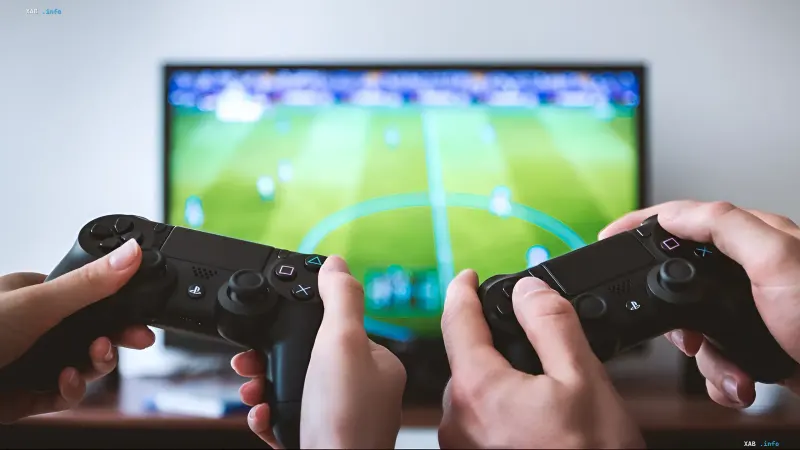 Две пары рук держат геймпады PlayStation на фоне телевизора с футбольной игрой