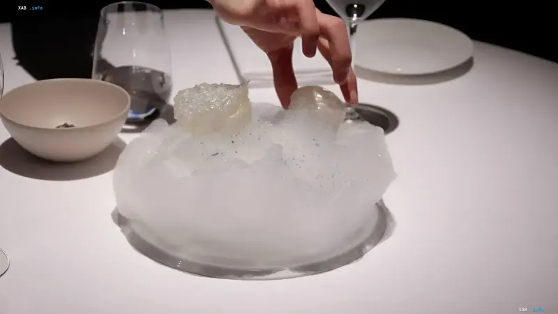 A waiter hand serves an exquisite cloud-like dish on a white restaurant table