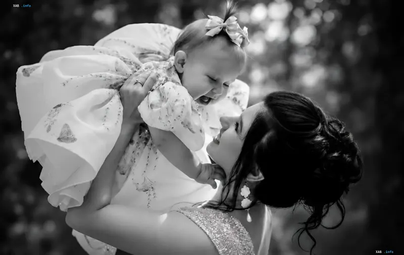 A mother tenderly holding her little daughter in a festive dress outdoors