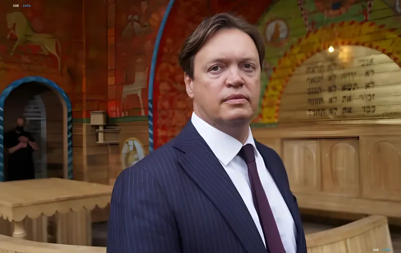 Ein Mann in einem dunkelblauen Nadelstreifenanzug und burgunderroter Krawatte vor dem Hintergrund traditioneller Bemalung