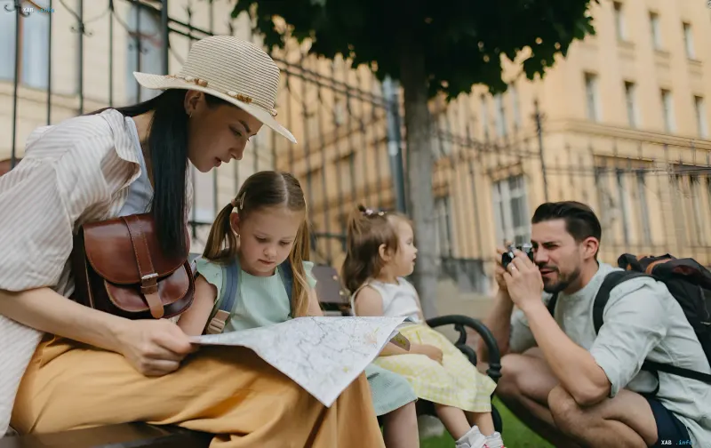 Family with children sitting on a bench in a European city and studying a map during a trip