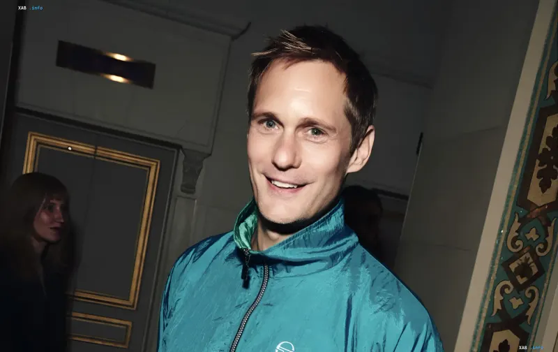 Alexander Skarsgard smiling on the red carpet wearing a blue sporty jacket