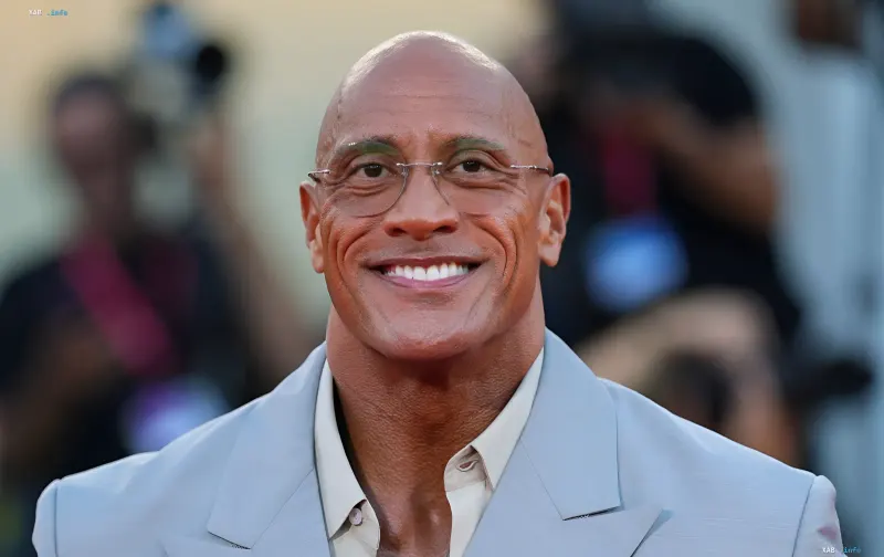 Dwayne The Rock Johnson wearing a grey-blue suit and glasses on a film set