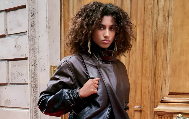 Junge lockige Model in einer braunen Lederjacke posiert vor einer Holztür