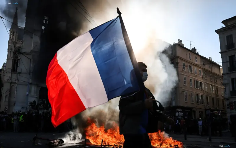 Protester holding a French flag against the backdrop of burning barricades and smoke during unrest