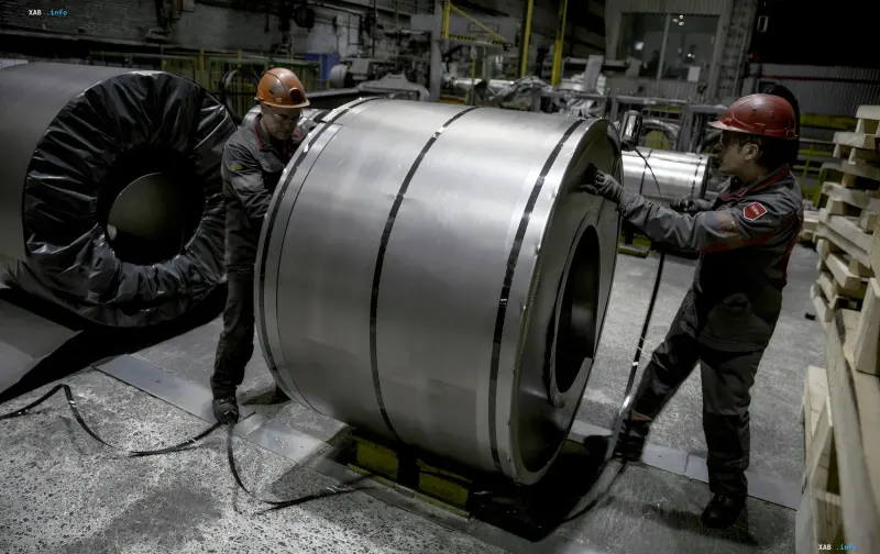 Workers in hard hats and overalls packing a steel coil at a metallurgical plant