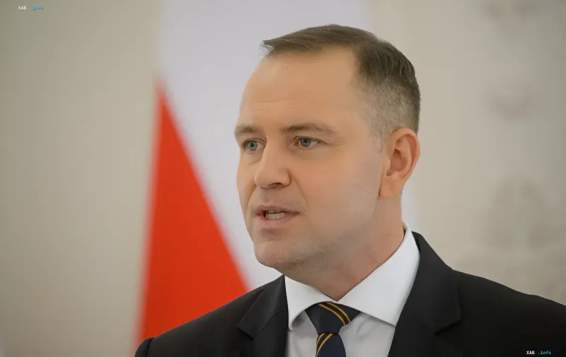 Polish political figure in a formal suit against the background of the Polish national flag