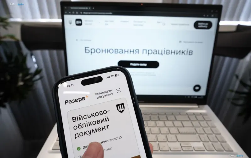 Смартфон с открытым электронным военно-учетным документом на фоне ноутбука с сайтом бронирования работников