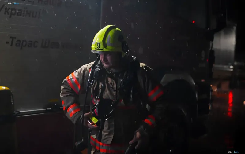 Пожарный в защитной каске и форме стоит у пожарной машины ночью во время дождя в Киеве