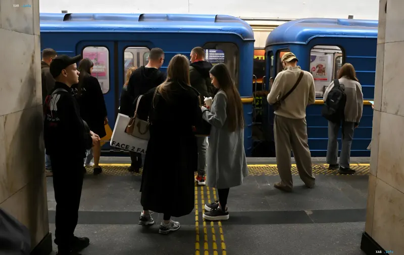 Passengers wait for a train at a capital subway station against the background of blue cars