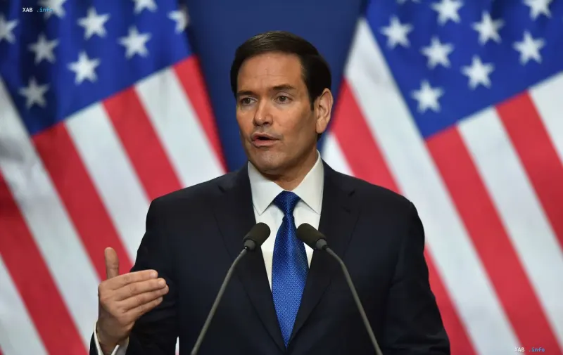 Госсекретарь США Марко Рубио выступает перед микрофонами на фоне американских флагов