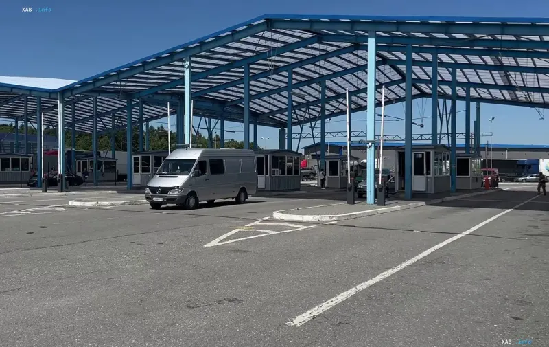 Автомобільний пункт пропуску із синім навісом та мікроавтобусом під ним на тлі ясного неба