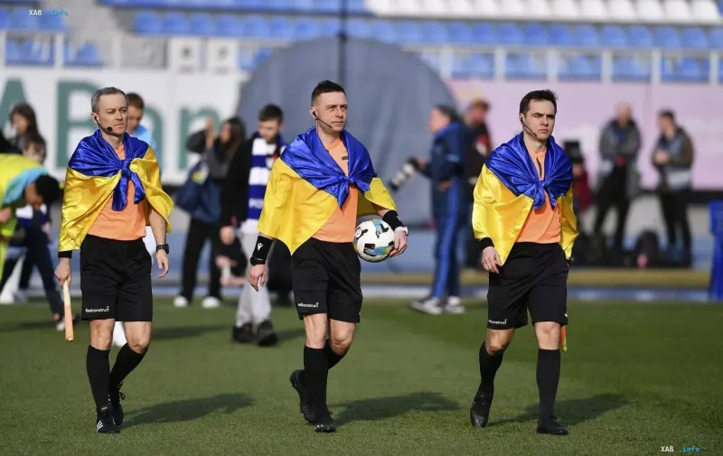 Судейская бригада в футболках с флагами Украины выходит на поле перед футбольным матчем