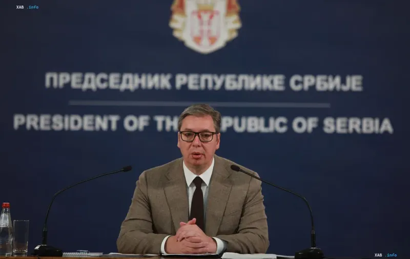 Бывший президент Сербии Александр Вучич выступает на пресс-конференции перед синим фоном с государственным гербом.