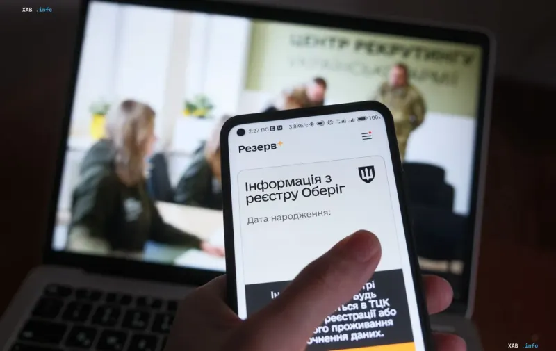 Смартфон с открытым приложением Резерв+ на фоне ноутбука в помещении