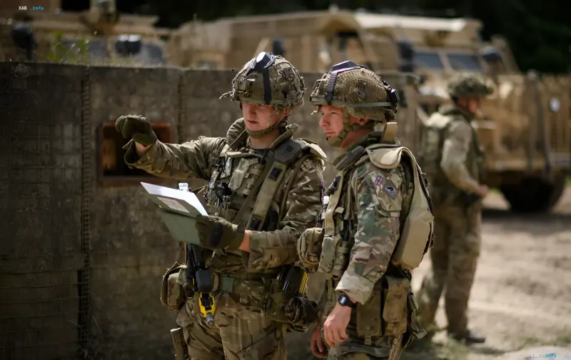 Two British soldiers in camouflage gear reviewing documents and a map during field exercises