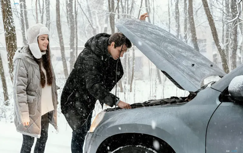 Driver in a winter jacket checks the engine of a broken-down car during a snowfall