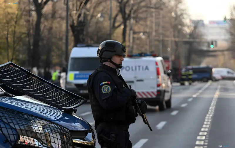 Romanian special forces operative in helmet and gear patrolling a street past police vehicles