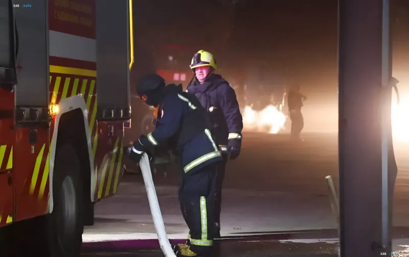 Feuerwehrleute mit Helmen an einem Löschfahrzeug bei der Arbeit am nächtlichen Einsatzort in Kiew