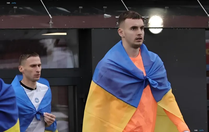 Fussballspieler im orangen Trikot mit der ukrainischen Flagge auf den Schultern im Stadion