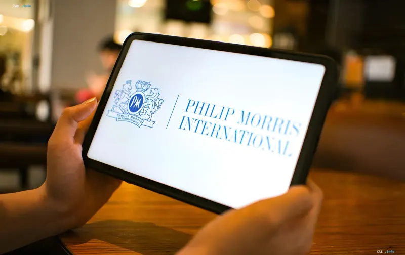 Руки держат планшет с логотипом Philip Morris International на экране в помещении
