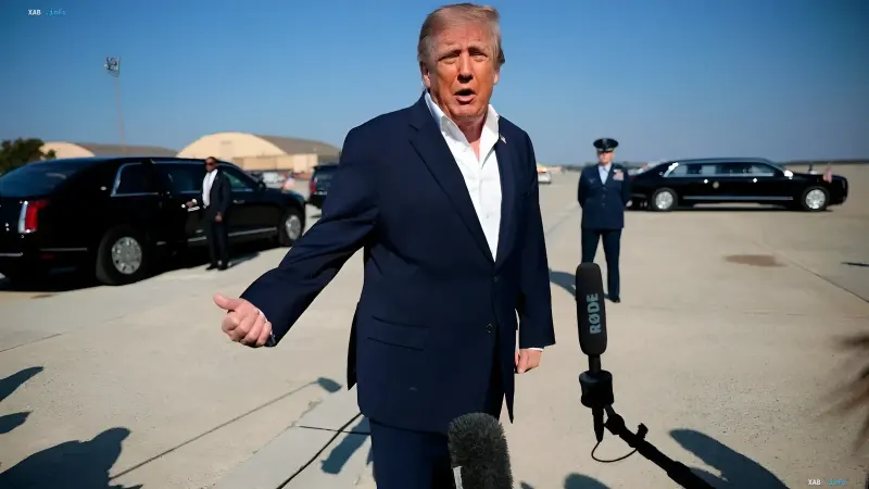 Дональд Трамп в темно-синем костюме дает интервью журналистам на аэродроме рядом с черными лимузинами