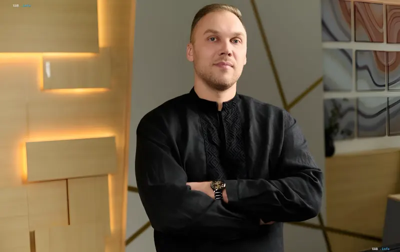 CEO компании SharksCode Антон Асеев в тёмной вышиванке со скрещенными руками на фоне современного офиса