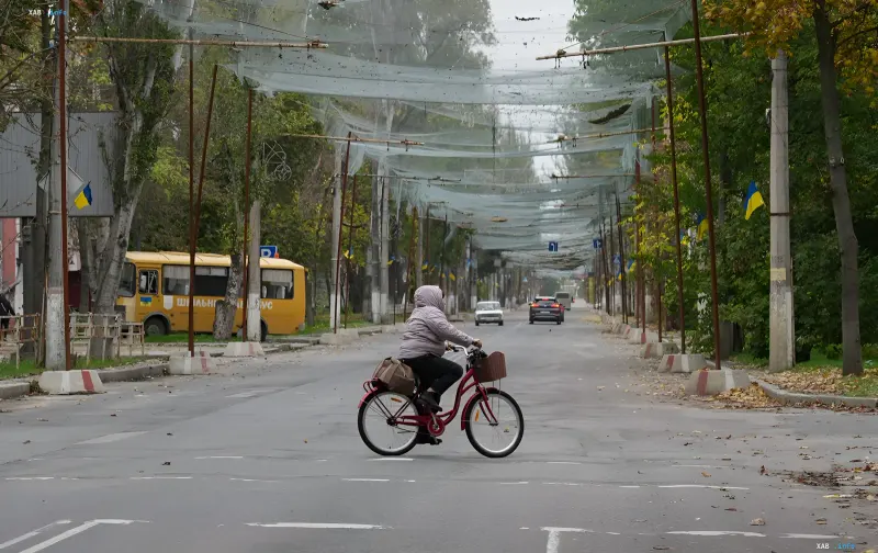 Eine Frau fährt mit dem Fahrrad auf einer leeren Straße einer ukrainischen Stadt mit Tarnnetzen über der Straße