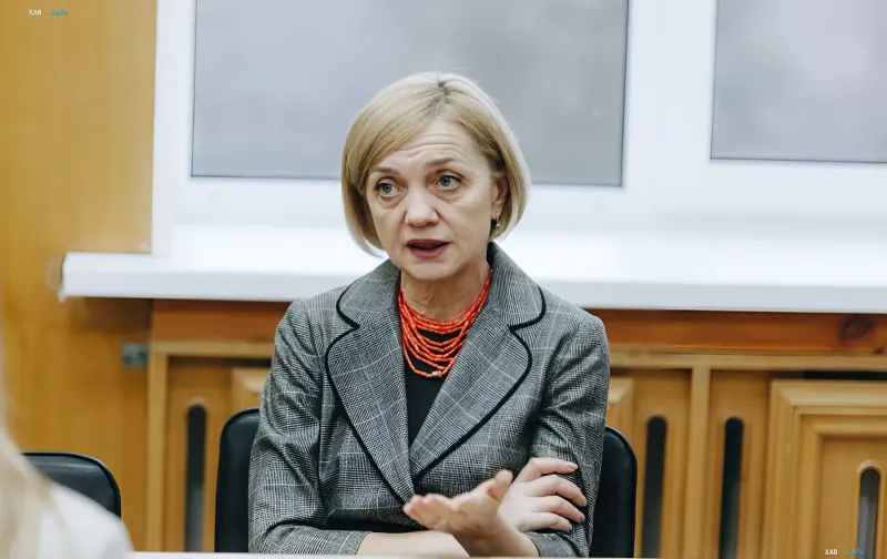 Woman in a business suit and red beads speaking during a press conference