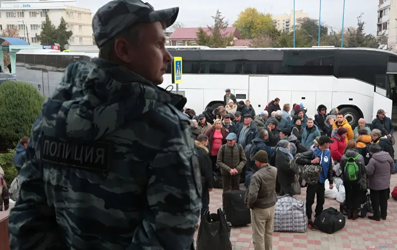 Российский полицейский и группа местных жителей с багажом у автобусов во время эвакуации