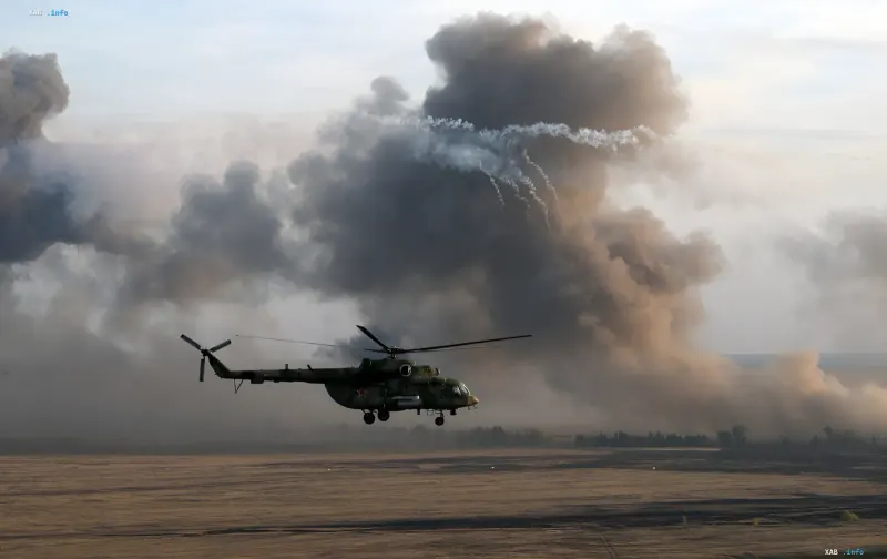 Военный вертолет Ми-8 совершает полет над открытой местностью на фоне густого дыма после удара дрона