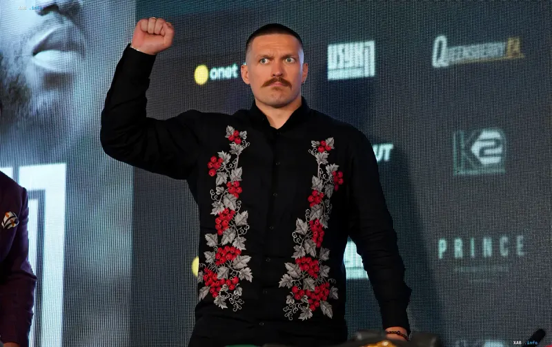 Украинский боксер Александр Усик в черной вышиванке поднимает кулак на пресс-конференции