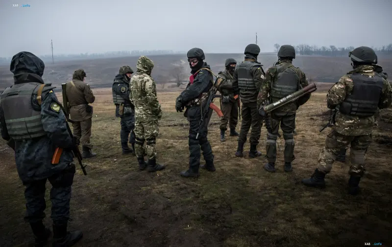 Armed Ukrainian servicemen in camouflage uniforms and helmets stand against an open landscape background