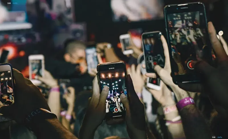 A crowd of people at a concert holding up smartphones to record video in the dark