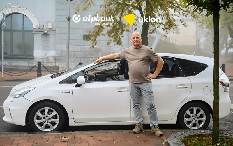 Водитель Uklon стоит рядом со своим белым автомобилем Toyota Prius на улице города