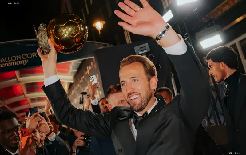 Harry Kane holding the Ballon d'Or trophy high and waving at the awards ceremony