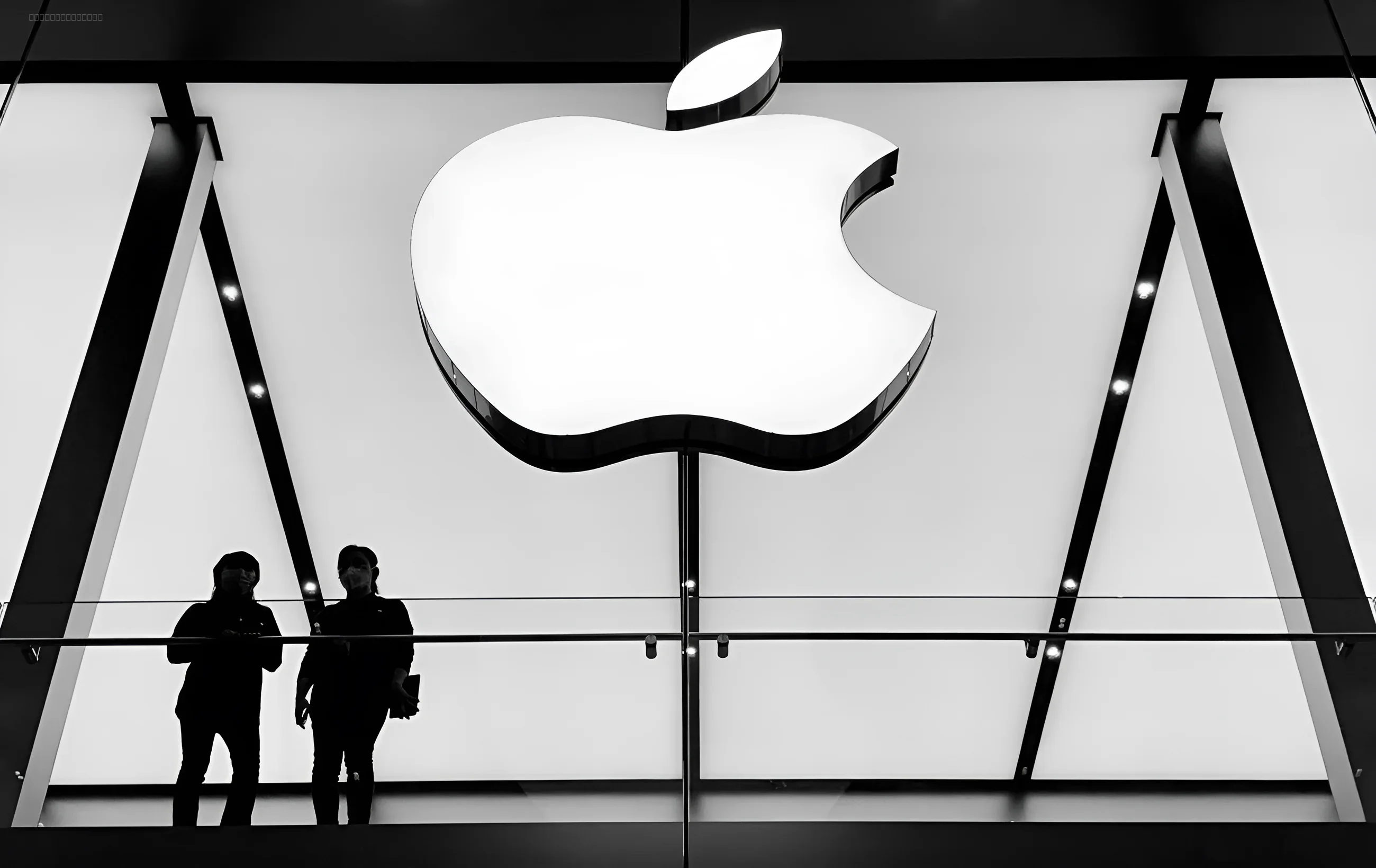 Логотип Apple на фоні скляної стіни з силуетами людей знизу — символ тестування нових версій iOS