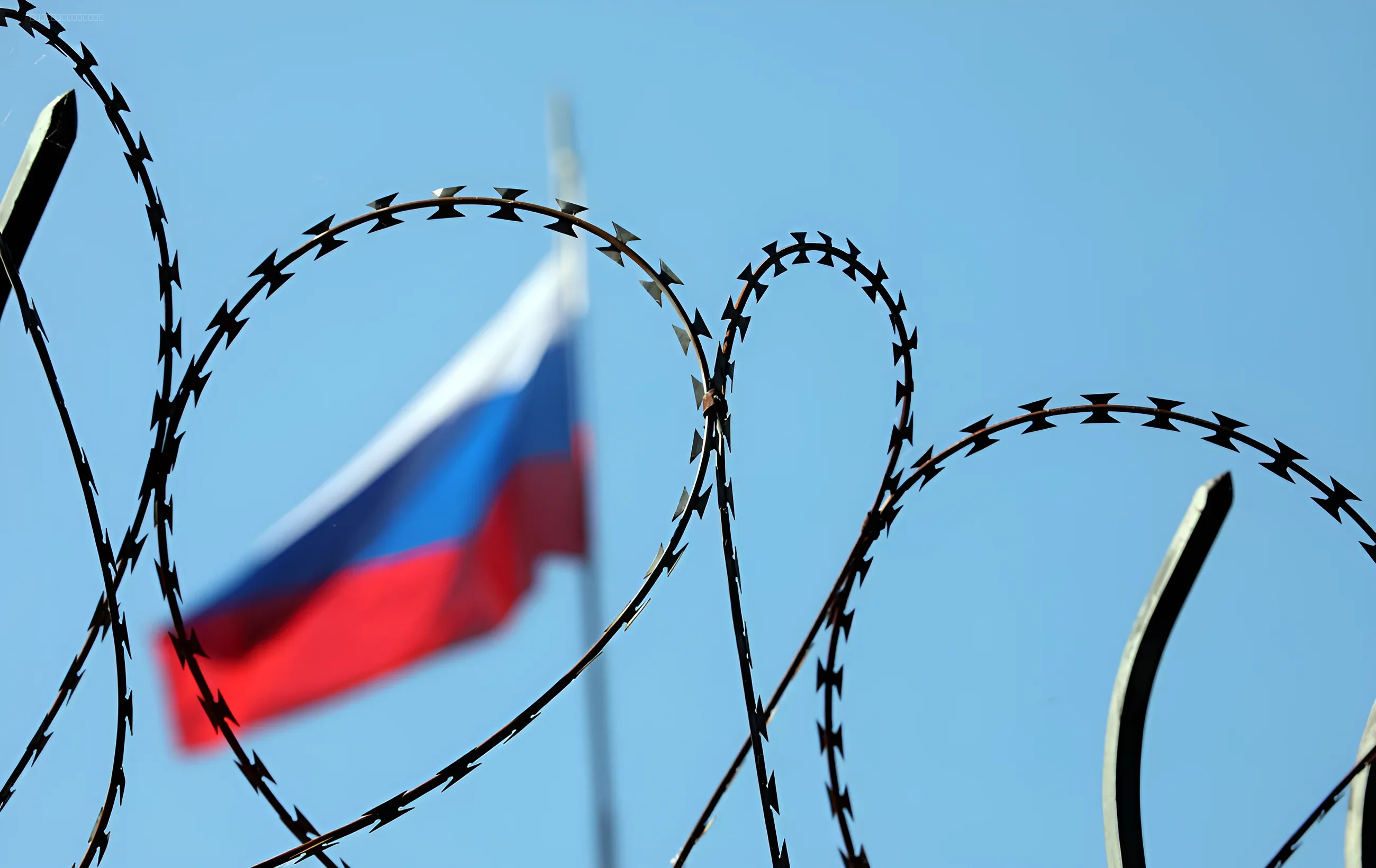 Российский флаг за колючей проволокой, символизирующий экономические санкции и изоляцию