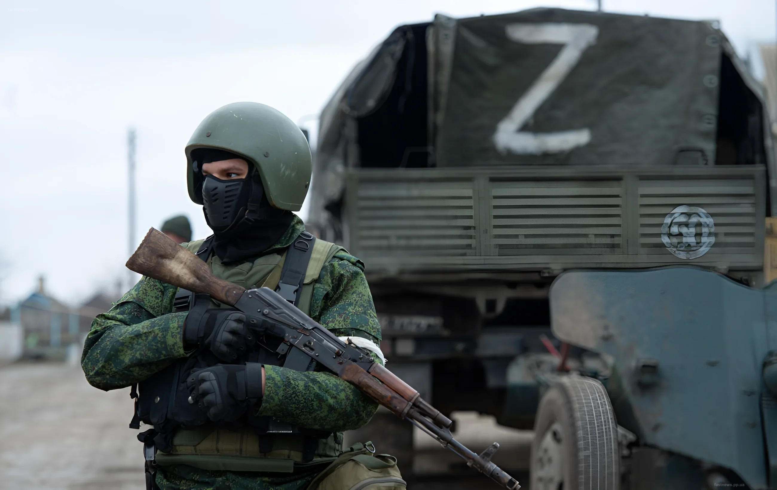 Russian soldier in camouflage and mask standing with a rifle against the background of a military vehicle with the letter Z