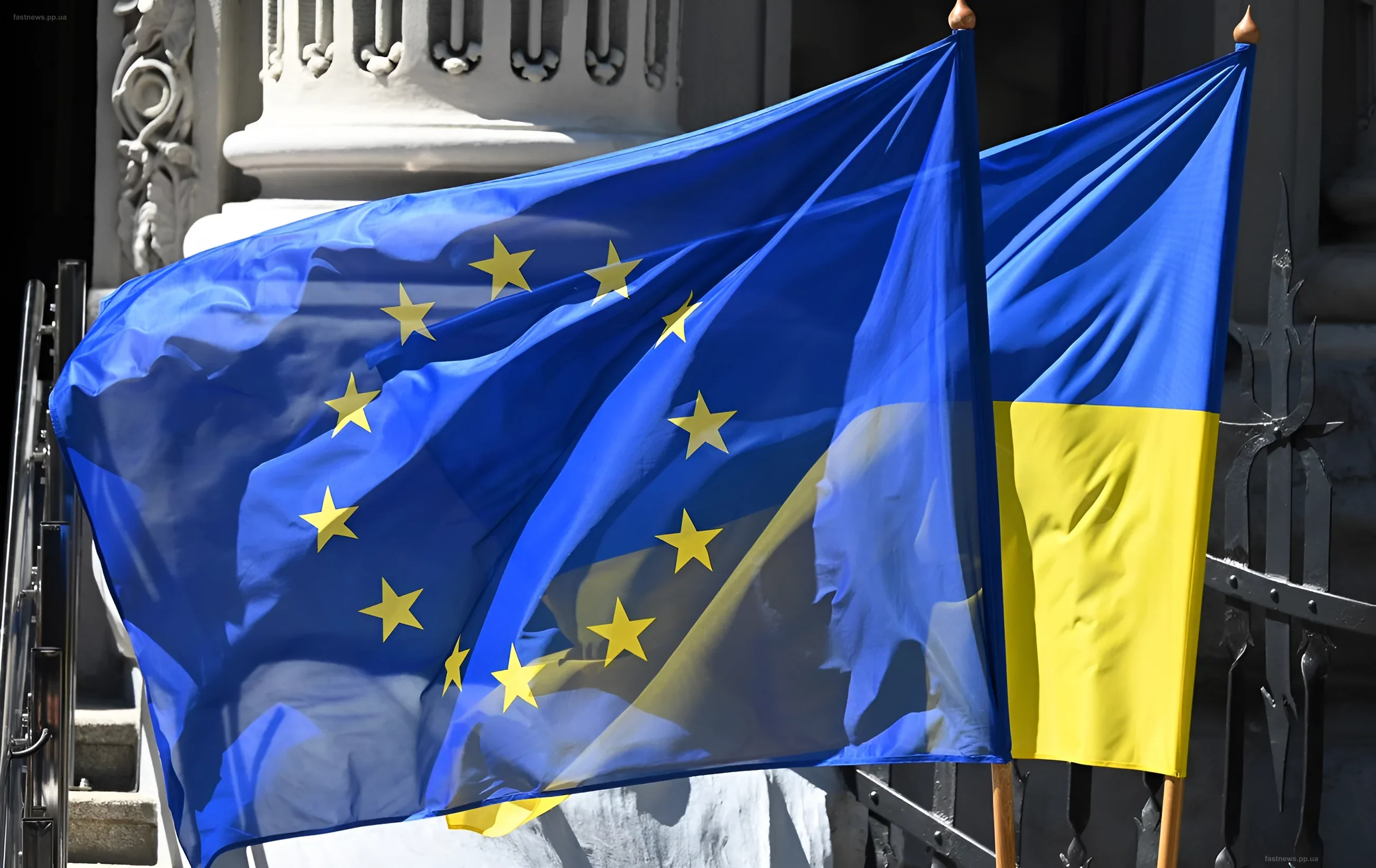 Флаг Европейского Союза и флаг Украины развеваются рядом на фоне здания, символизируя начало переговоров о вступлении.