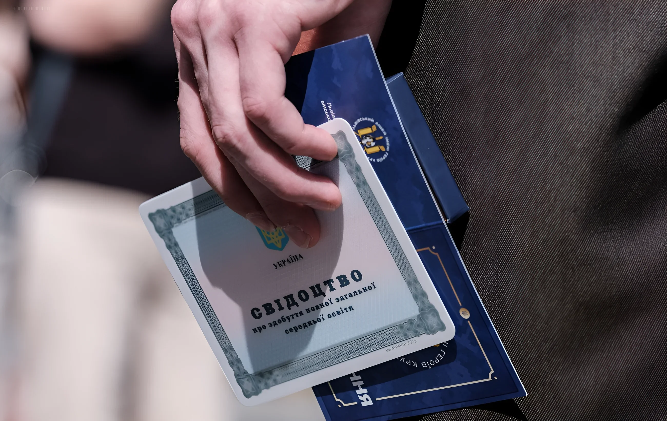 Ручка держит новый украинский диплом о высшем образовании с синей обложкой и гербом