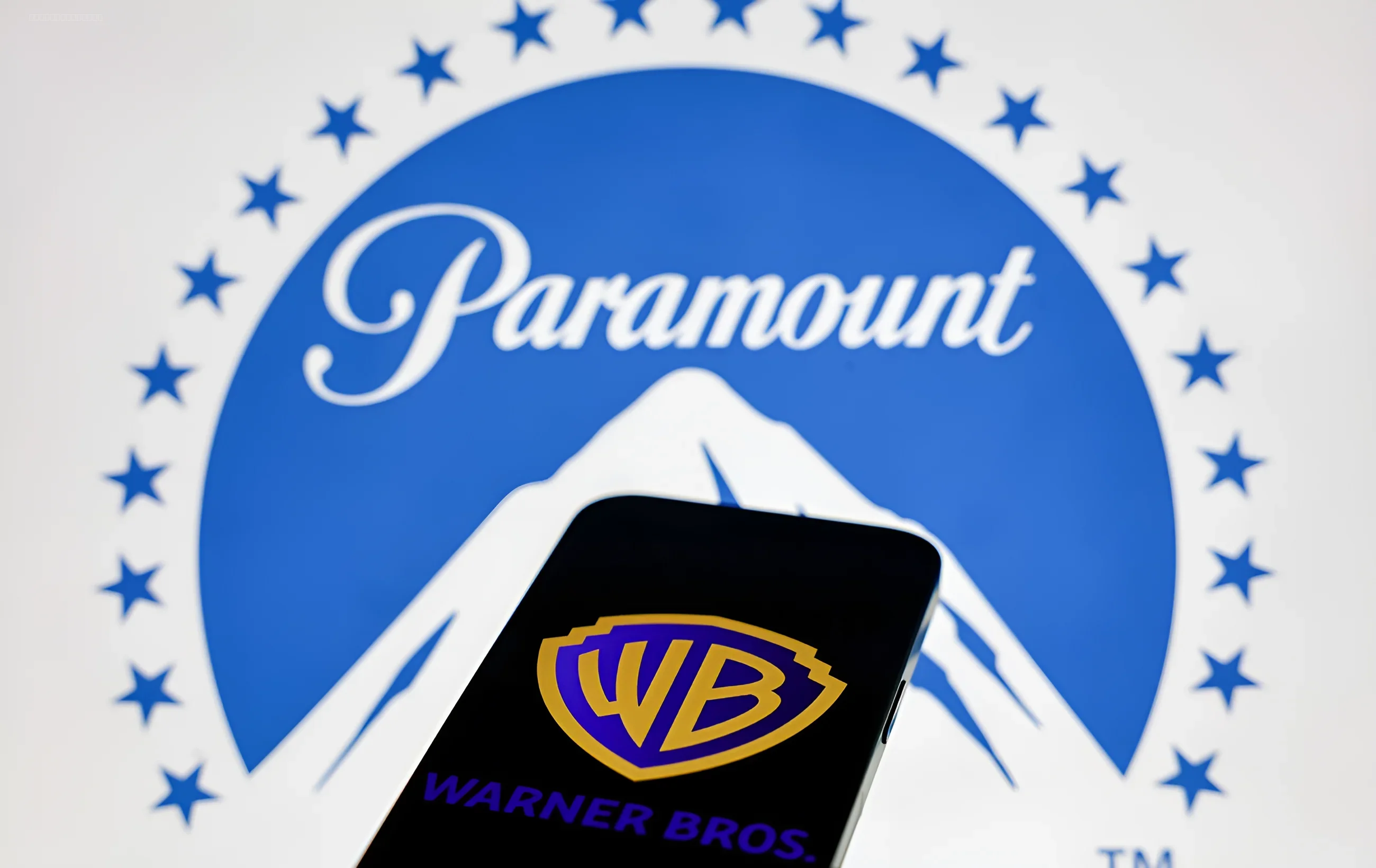 Логотипы Paramount и Warner Bros на фоне смартфона, символизирующие слияние медиагигантов